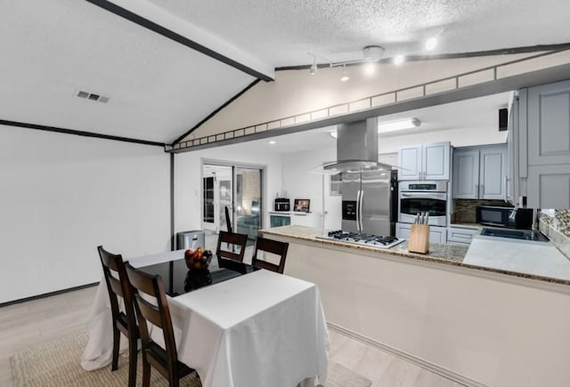 kitchen featuring stainless steel appliances, lofted ceiling with beams, a textured ceiling, gray cabinets, and island range hood