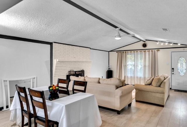 living room with a brick fireplace, vaulted ceiling with beams, ceiling fan, a textured ceiling, and light hardwood / wood-style floors