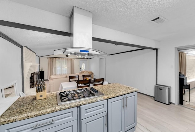 kitchen with island range hood, stone countertops, a textured ceiling, and stainless steel gas cooktop