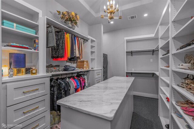 spacious closet with dark colored carpet and an inviting chandelier