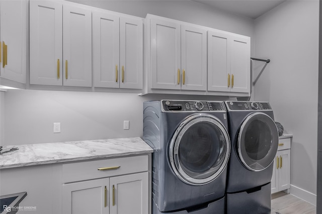 clothes washing area with cabinets, light wood-type flooring, and washer and dryer