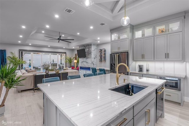 kitchen featuring light stone countertops, sink, a spacious island, a tray ceiling, and appliances with stainless steel finishes