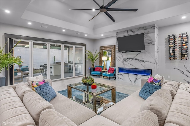 living room featuring a premium fireplace, a raised ceiling, and ceiling fan