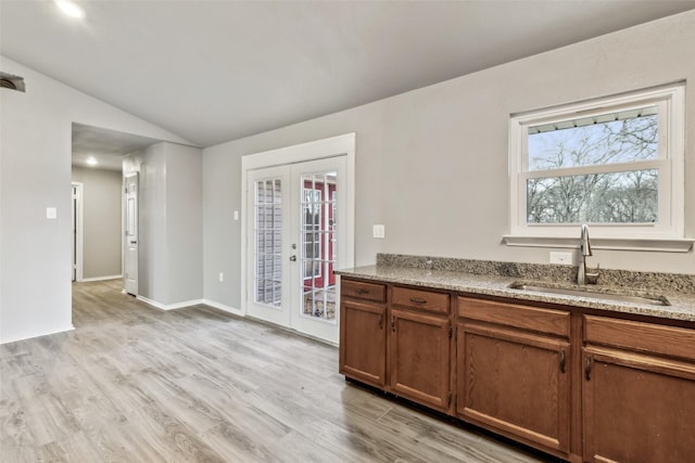 kitchen featuring french doors, sink, vaulted ceiling, light wood-type flooring, and light stone counters