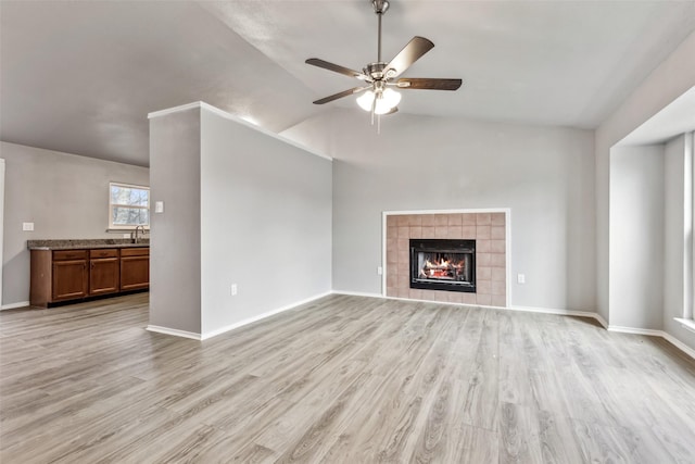 unfurnished living room with lofted ceiling, sink, light hardwood / wood-style flooring, ceiling fan, and a tiled fireplace