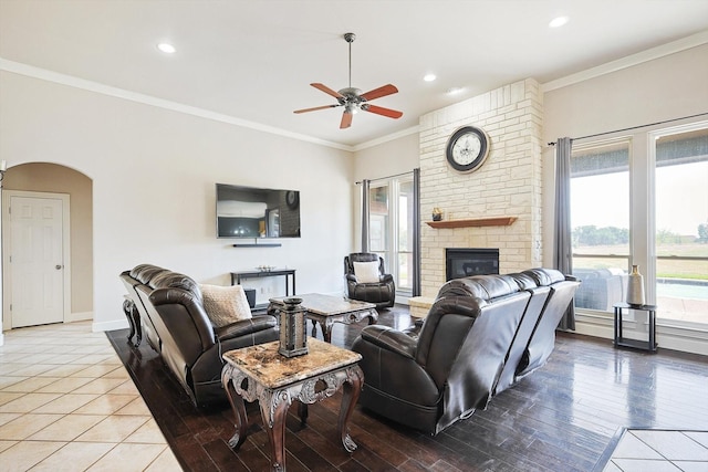 living room with crown molding, a fireplace, ceiling fan, and light wood-type flooring