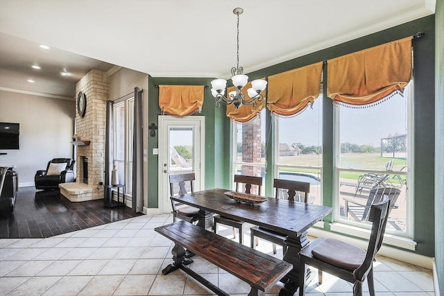 dining room featuring an inviting chandelier, a brick fireplace, crown molding, and light tile patterned flooring