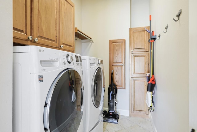 clothes washing area featuring separate washer and dryer, light tile patterned floors, and cabinets