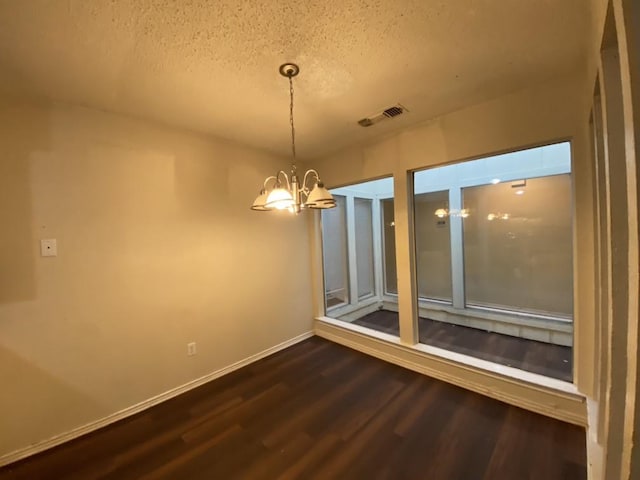 unfurnished dining area featuring hardwood / wood-style flooring, a textured ceiling, and an inviting chandelier