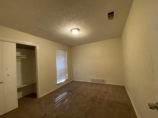 unfurnished bedroom with dark colored carpet, a textured ceiling, and a closet