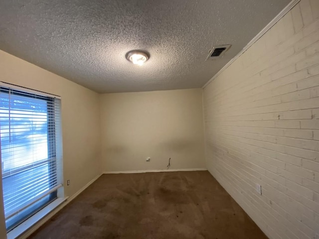 spare room featuring a textured ceiling, dark carpet, and brick wall