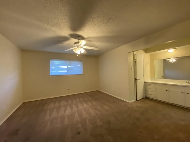 unfurnished bedroom featuring ceiling fan, sink, dark colored carpet, ensuite bathroom, and a textured ceiling