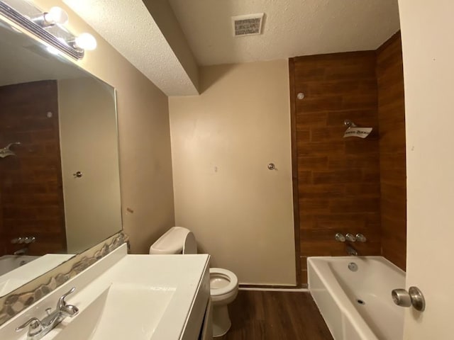 full bathroom with hardwood / wood-style floors, a textured ceiling, toilet, vanity, and bathtub / shower combination