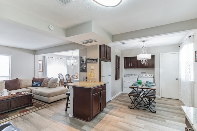 kitchen with washer and clothes dryer, hanging light fixtures, a kitchen island, white fridge, and a breakfast bar area