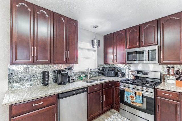 kitchen featuring light stone countertops, appliances with stainless steel finishes, backsplash, sink, and pendant lighting