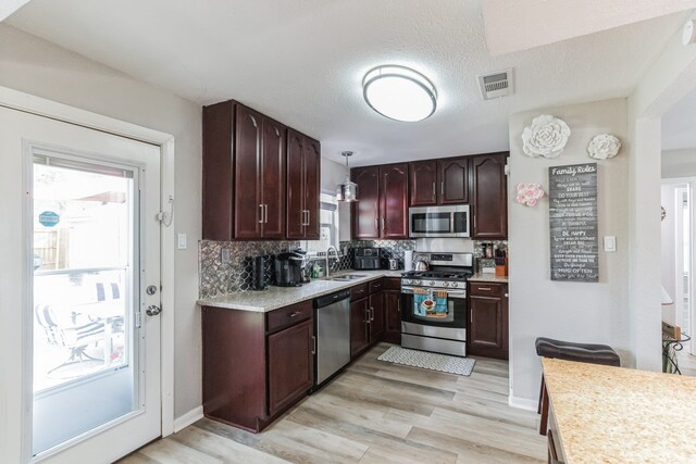 kitchen with dark brown cabinetry, backsplash, appliances with stainless steel finishes, ceiling fan with notable chandelier, and light wood-type flooring