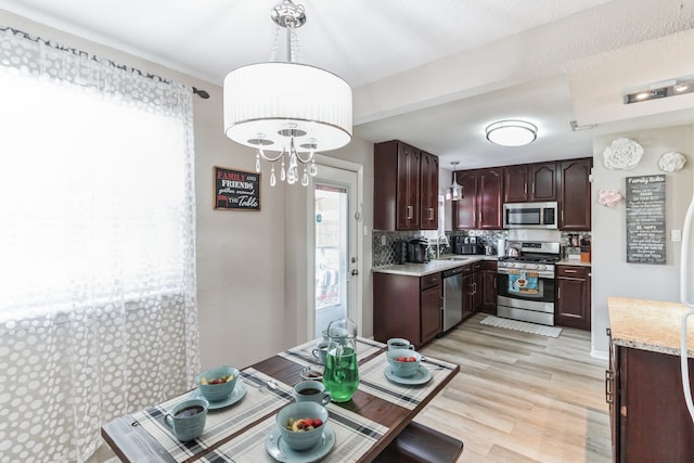 kitchen featuring hanging light fixtures, sink, light hardwood / wood-style flooring, appliances with stainless steel finishes, and tasteful backsplash