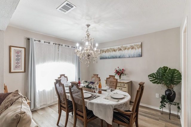 dining space featuring a notable chandelier, light hardwood / wood-style floors, and a textured ceiling