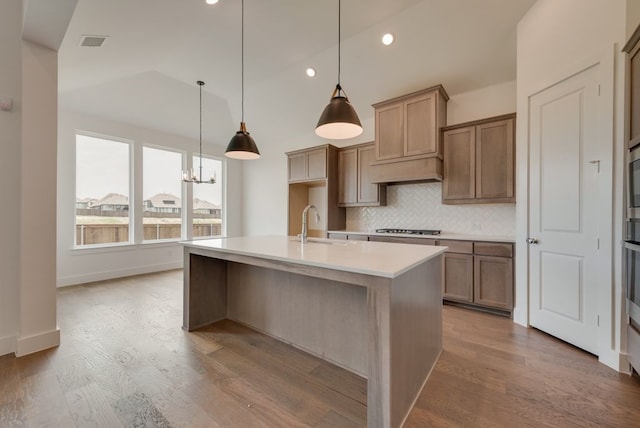 kitchen with pendant lighting, a kitchen island with sink, sink, wood-type flooring, and gas cooktop