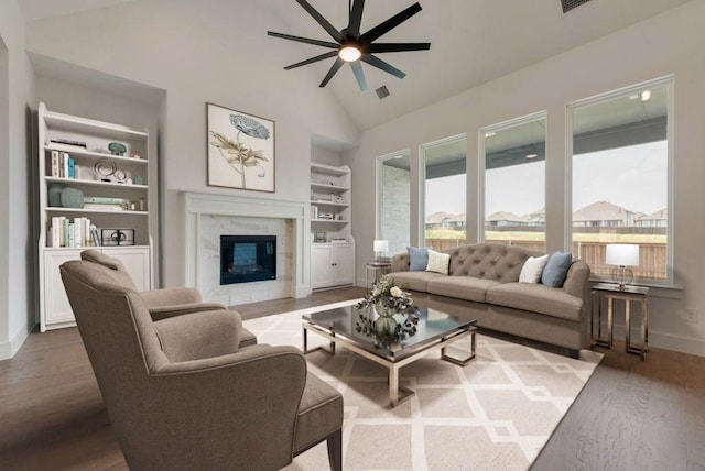 living room featuring hardwood / wood-style floors, built in features, high vaulted ceiling, ceiling fan, and a premium fireplace