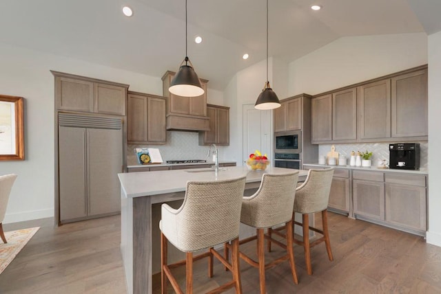 kitchen featuring pendant lighting, a center island with sink, vaulted ceiling, built in appliances, and tasteful backsplash