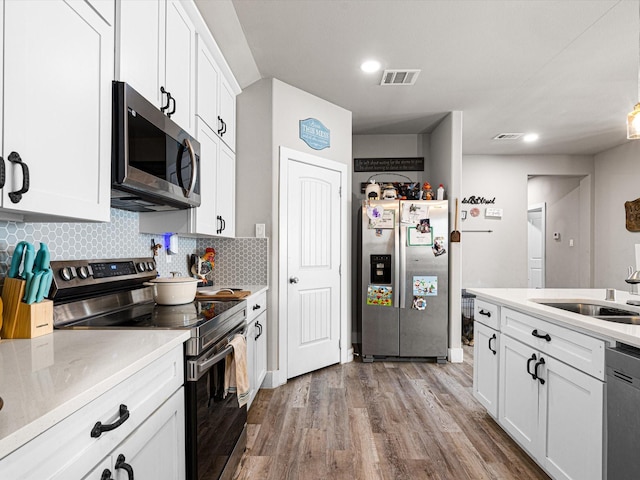 kitchen featuring sink, white cabinets, hardwood / wood-style floors, tasteful backsplash, and appliances with stainless steel finishes