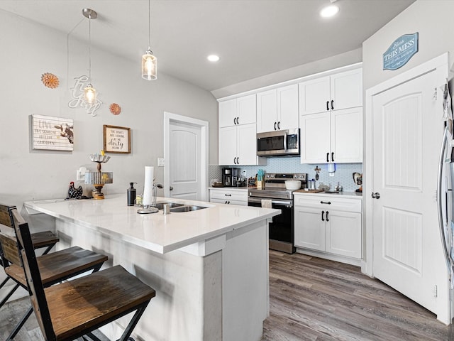 kitchen featuring a breakfast bar, appliances with stainless steel finishes, kitchen peninsula, pendant lighting, and white cabinets