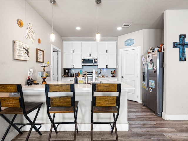 kitchen featuring hanging light fixtures, stainless steel appliances, a breakfast bar, and white cabinets