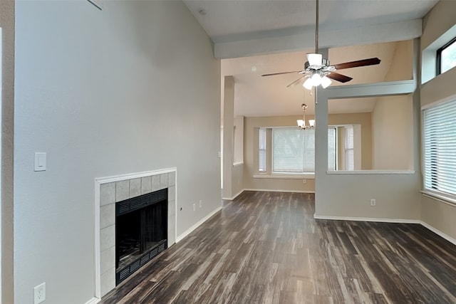 unfurnished living room featuring a wealth of natural light, ceiling fan with notable chandelier, a tile fireplace, and dark wood-type flooring