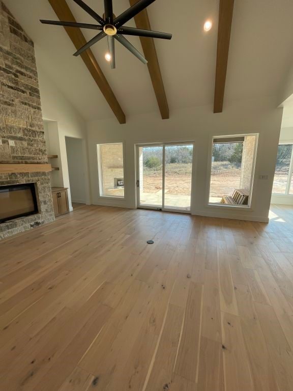 unfurnished living room featuring high vaulted ceiling, ceiling fan, built in shelves, a fireplace, and light hardwood / wood-style floors