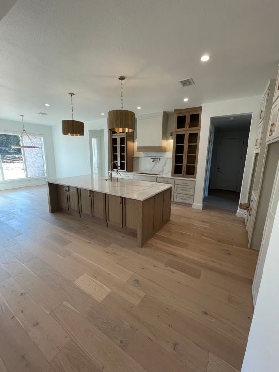 kitchen with custom exhaust hood, sink, a large island with sink, light hardwood / wood-style flooring, and hanging light fixtures