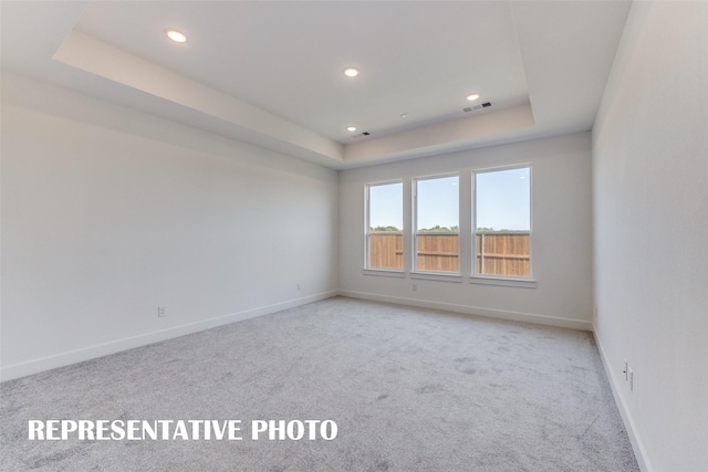 empty room with a raised ceiling and light carpet