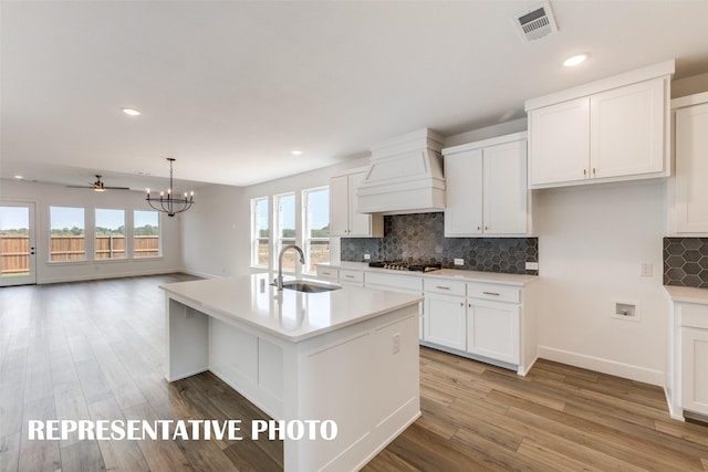 kitchen featuring sink, an island with sink, hanging light fixtures, and custom exhaust hood