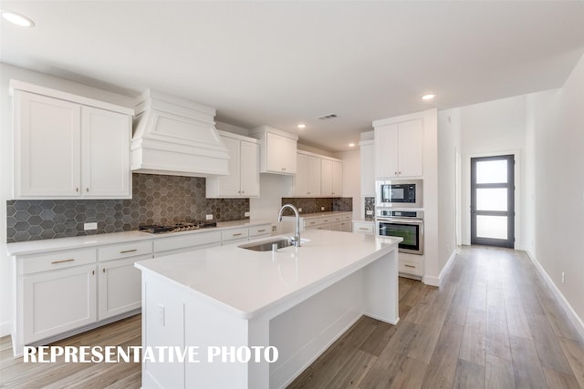 kitchen featuring premium range hood, sink, white cabinetry, an island with sink, and stainless steel appliances