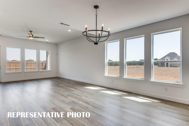 unfurnished dining area featuring ceiling fan with notable chandelier, a wealth of natural light, and light hardwood / wood-style flooring