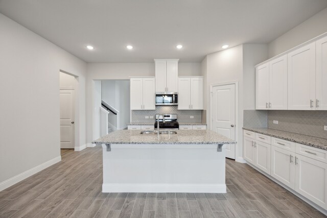 kitchen with light stone countertops, white cabinetry, an island with sink, and stainless steel appliances