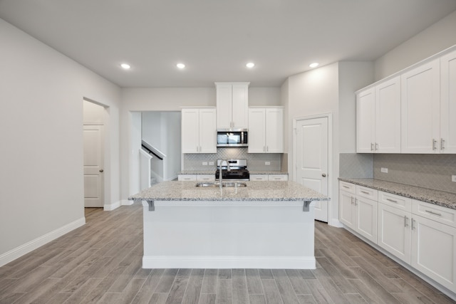 kitchen with stainless steel appliances, a kitchen island with sink, white cabinets, and light stone counters