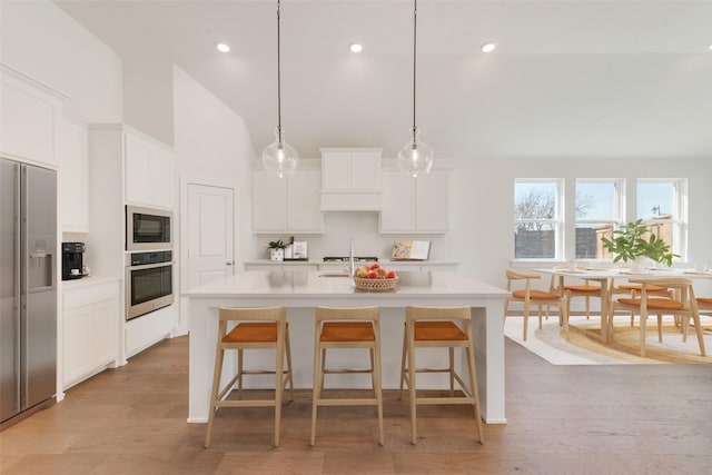 kitchen with an island with sink, appliances with stainless steel finishes, white cabinets, and decorative light fixtures