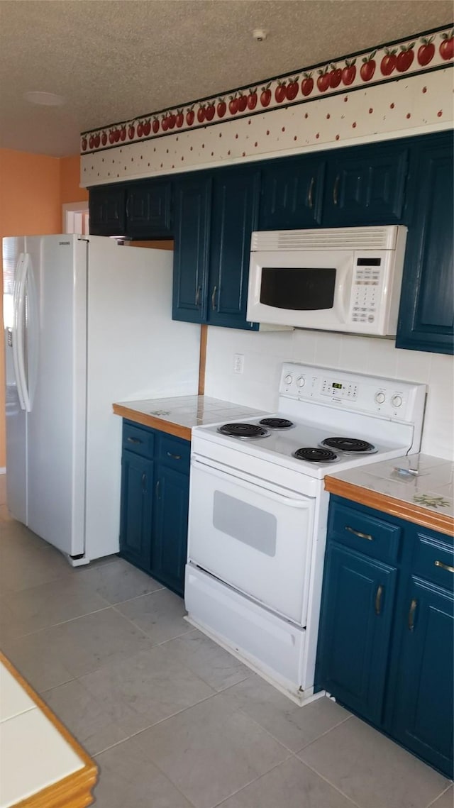 kitchen featuring light tile patterned flooring, blue cabinetry, a textured ceiling, and white appliances