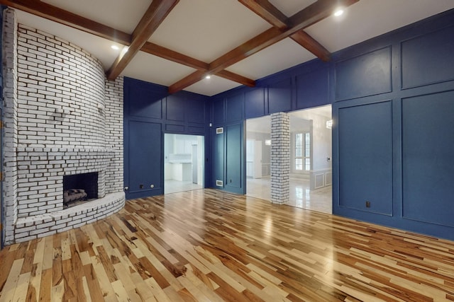 unfurnished living room with coffered ceiling, a brick fireplace, ornate columns, beamed ceiling, and light hardwood / wood-style floors