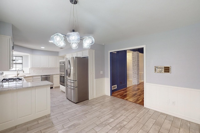 kitchen with kitchen peninsula, appliances with stainless steel finishes, decorative light fixtures, white cabinets, and light hardwood / wood-style floors