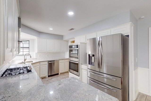 kitchen with white cabinetry, sink, light stone counters, decorative backsplash, and appliances with stainless steel finishes