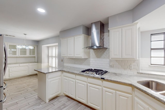 kitchen featuring wall chimney exhaust hood, pendant lighting, a chandelier, white cabinetry, and stainless steel gas stovetop