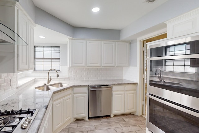 kitchen with decorative backsplash, appliances with stainless steel finishes, light stone counters, sink, and white cabinetry