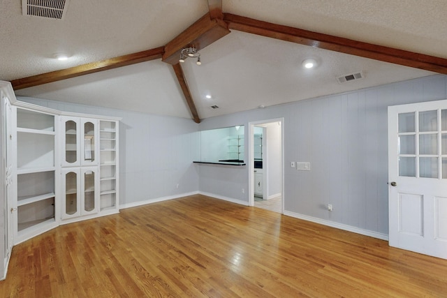 unfurnished living room featuring a textured ceiling, lofted ceiling with beams, and light hardwood / wood-style flooring