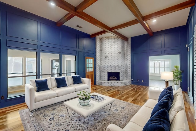 living room featuring beamed ceiling, light hardwood / wood-style flooring, a fireplace, and coffered ceiling