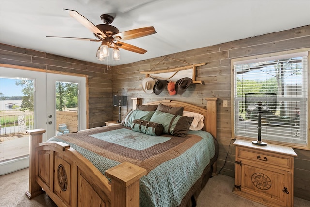 carpeted bedroom featuring ceiling fan, access to exterior, wooden walls, and french doors