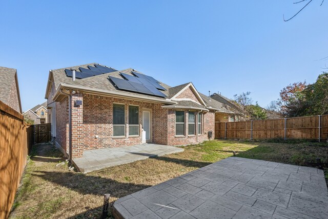 rear view of property featuring solar panels, a lawn, and a patio area