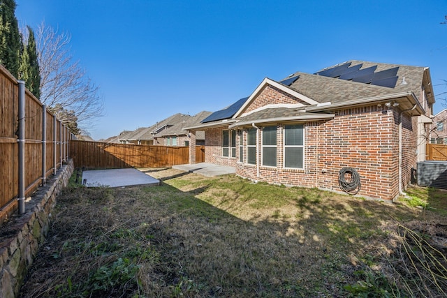 rear view of property featuring a lawn, a patio, and solar panels