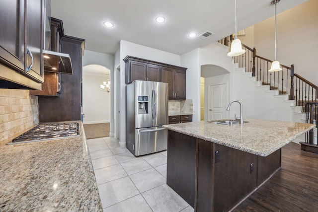 kitchen featuring pendant lighting, sink, stainless steel appliances, light stone counters, and an island with sink